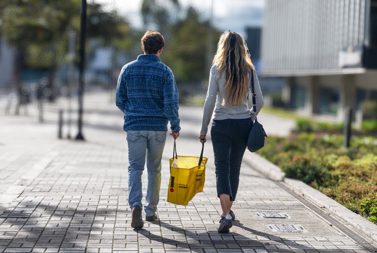 Young couple walking through city holding tote bag>