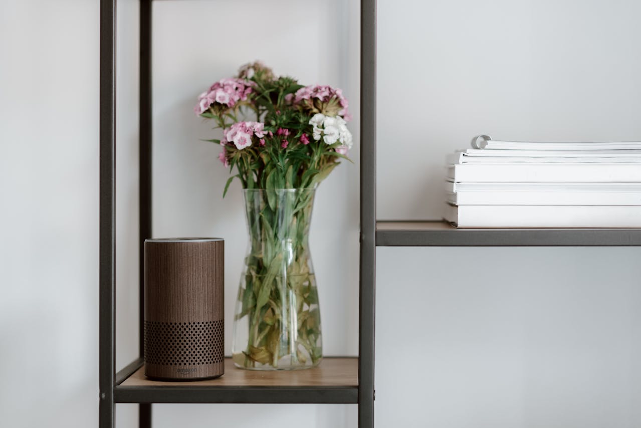 A minimal shelf with flowers in a vase and a smart speaker