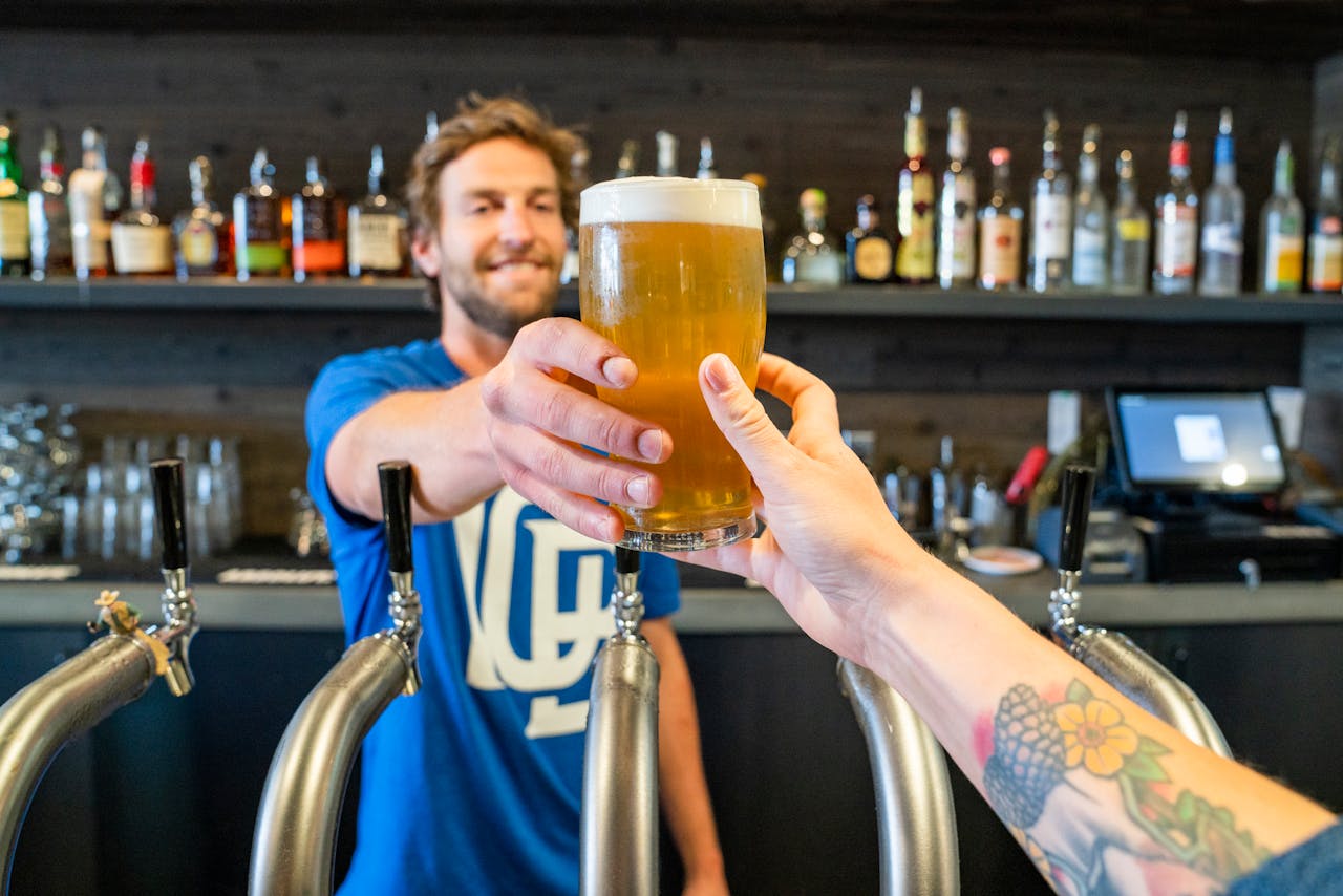 Bar tender shown handing glss of beer to an outstretched hand