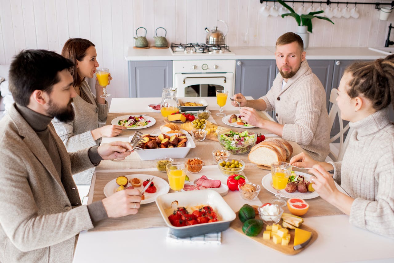 A group of people are seated at a large wood table enjoying a meal together