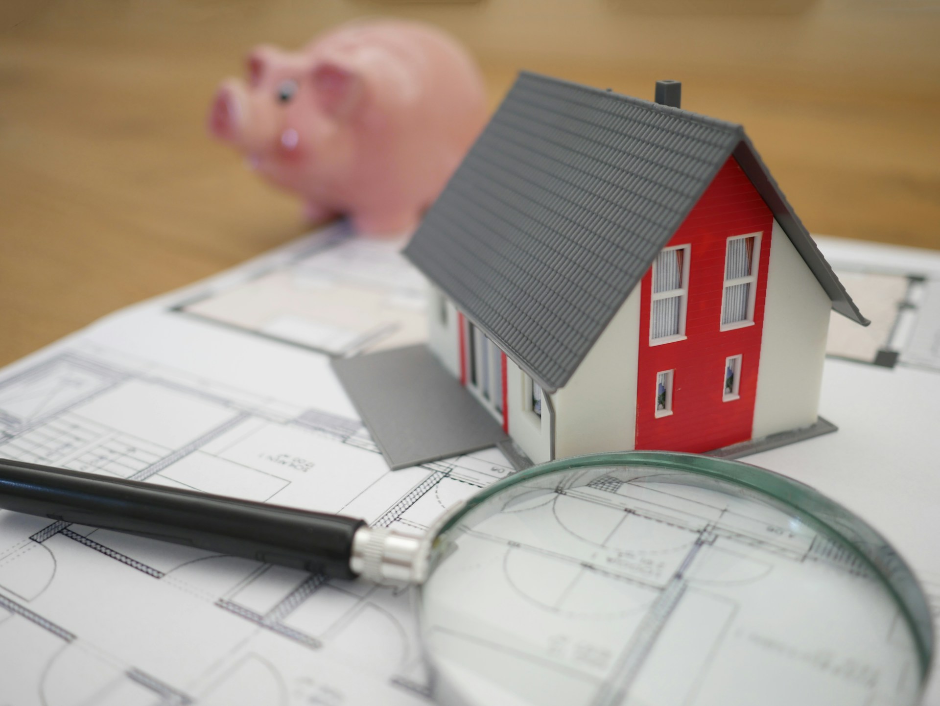 White and red house over a blueprint with piggy bank in the background>